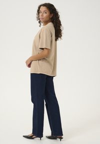 T-shirt en coton beige à manches courtes, associé à un jean large bleu foncé. Les deux ont une coupe décontractée et peu de détails. Chaussures noires à bouts pointus.