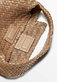 Sac à main en cuir tissé de couleur marron clair avec des étiquettes rectangulaires cousues, dont une estampillée "Massimo Dutti", sur fond blanc.