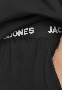 Czarna bawełniana tkanina z fakturowanym pasem, na którym widnieje napis "JACK & JONES" w białym kolorze. Projekt charakteryzuje się gładkim wykończeniem i delikatnie układa się na ciele.
