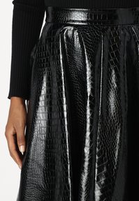 Falda negra con pliegues y textura de cocodrilo brillante, con una cinturilla ajustada y una silueta en A.