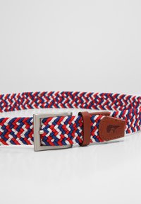 Spleciony pasek z czerwonymi, białymi i niebieskimi włóknami bawełnianymi, z metalową klamrą w kolorze srebra oraz brązowymi skórzanymi akcentami i brandingiem.