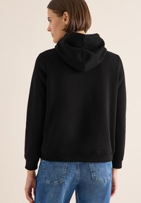 Sudadera con capucha negra de textura suave, con un corte holgado, puños de canalé y un diseño en color sólido. Combinada con jeans de mezclilla azul claro.