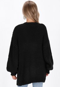 Svart stickad tröja med lös passform, nedhasade axlar och strukturerade stygn. Har en rundad halsringning och långa, luftiga ärmar.