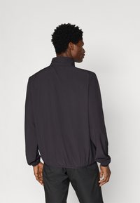 Giacca nera leggera con colletto alto, vita elastica e maniche lunghe. Texture liscia, senza motivi visibili o dettagli hardware.