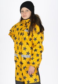 Geel waterdichte regenjas met zwart sterrenpatroon, elastische manchetten en reflecterende strips. Combineer met bijpassende shorts voor een complete look.