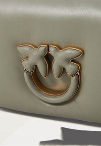 Groene leren handtas met een goudkleurig metalen handvat in de vorm van een glimlachend gezicht, versierd met vlinderaccenten. Vlotte textuur met een gestructureerd ontwerp.