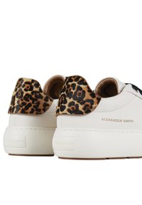 Hvide lædersneakers med en leopardmønstret hælflap, der har en gummisål og gyldent "ALEXANDER SMITH" branding.