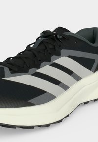 Μαύρο και γκρι αθλητικό παπούτσι με λευκό σχέδιο τριών ρίγων, μαύρα κορδόνια, μαξιλαρωμένο κολάρο και παχύ λευκό πέλμα με υφή για καλύτερη πρόσφυση.