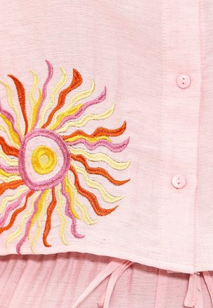 Tissu rose avec un design brodé de soleil présentant des vagues orange, jaunes et roses. Des boutons roses sur le vêtement ajoutent du détail.