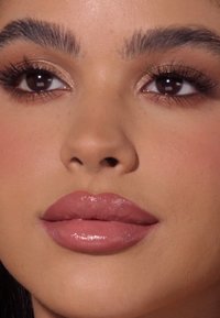 Zbliżenie twarzy z gładkimi, pełnymi ustami o błyszczącym, cielistym wykończeniu, dobrze zdefiniowanymi brwiami i delikatnie podkreśloną karnacją.