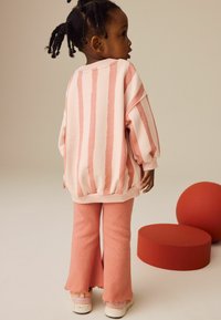 Lys rosa stribet sweatshirt med oversized ærmer og matchende rosa flared bukser. Tilbehøret inkluderer lyse sko med en spottet sål.