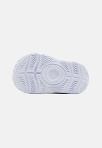 Kengän pohja, jossa on aaltoileva kuviointi ja keskellä ympyrälogo, valmistettu teksturoidusta valkoisesta kumista.