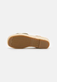 Espadrille with a woven jute sole, olive green textile upper, rubberized brown accents, and a textured, wavy tread pattern on the sole.