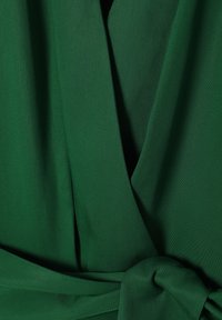 Rochie verde dintr-un material neted. Prezintă un decolteu adânc în V și detalii legate la talie. Textură moale cu o ușoară strălucire.