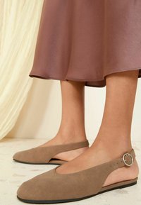 Ballerine beige con punta rotonda, texture in morbido suede, ritagli laterali e un accento in metallo argentato sulla cinghia del tallone.