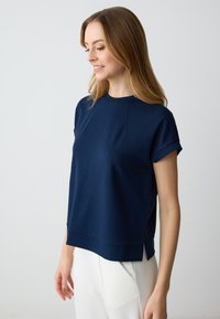Top blu navy a maniche corte con scollatura rotonda, caratterizzato da spacchi laterali e una texture liscia e elastica per il massimo comfort. Vestibilità sagomata.