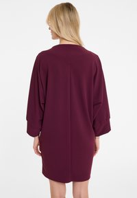 Bordeauxfarbenes Kleid mit lässiger Passform, ausgestattet mit einem runden Ausschnitt und weiten Fledermausärmeln. Glattes Material in einfarbiger Ausführung mit minimalistischem Design.