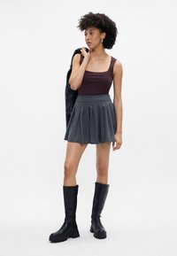 Μπορντό εφαρμοστό αμάνικο τοπ, γκρι πλισέ φούστα με ρίγες και μαύρες μπότες ως το γόνατο. Η φιγούρα κρατά επίσης μια μαύρη ζακέτα στον ώμο.