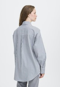 Gestreifte Button-up-Bluse in Blau und Weiß, mit langen Ärmeln, einem Kragen und einem abgerundeten Saum. Glattes Material mit taillierter Passform.