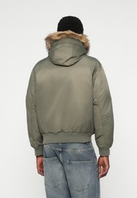 Olivroheline puffer-jakk faux karusnahaga voodriga kapuutsiga, ribatud mansettide ja äärega. Sile, isoleeritud kangas, millel on mugav lõige.