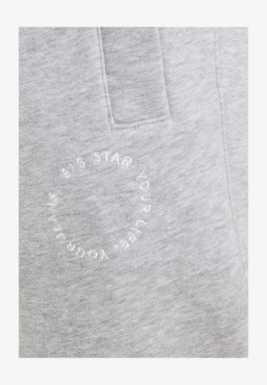 Hellgrauer Stoff mit einer aufgenähten Tasche und einem kreisförmigen weißen Sticktext, der "BIG STAR YOUR LIFE YOUR FRIENDS" lautet.