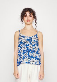 Top de alças spaghetti floral com um fundo azul e flores brancas, ajuste solto e tecido leve. Calções brancos simples.