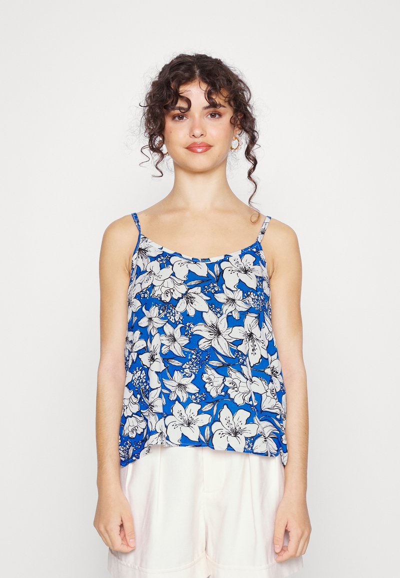 Top de alças spaghetti floral com um fundo azul e flores brancas, ajuste solto e tecido leve. Calções brancos simples.