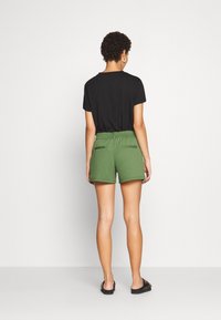 Černé tričko s krátkým rukávem ve spojení se zelenými šortkami s elastickým páskem, dvěma zadními kapsami a volnějším střihem.