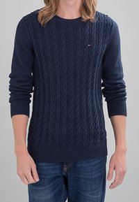 Maglione a maglia cable di colore blu navy con scollo rotondo e polsini a coste. Realizzato in tessuto morbido, presenta un piccolo logo sul petto.
