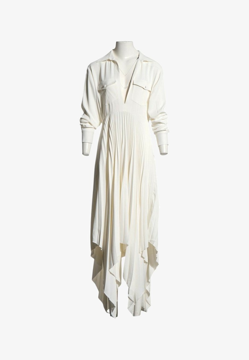 Longue robe blanche avec une jupe plissée, des manches longues, deux poches poitrine et un ourlet asymétrique sur un mannequin.