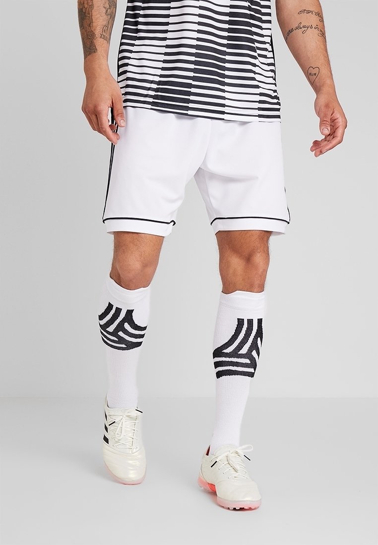 Pantalones cortos blancos con acentos negros, camiseta a rayas en blanco y negro, y calcetas blancas con un patrón de olas negras; zapatos de fútbol plateados metálicos.
