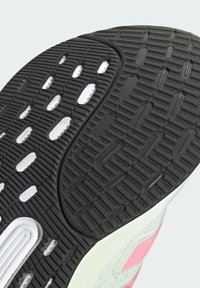 Suela de tenis de goma negra con patrones de agarre texturizados, con detalles en blanco y rosa y una sección verde lisa a lo largo del lateral.