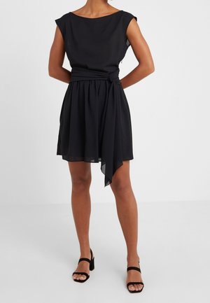 Czarna sukienka o luźnym kroju, z krótką spódnicą i asymetrycznym dołem. Posiada szeroki dekolt i ozdobne wiązanie w pasie. Gładka tekstura tkaniny.