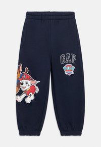 Marineblauwe joggingbroek met elastische tailleband, voorzien van kleurrijke cartoonhondenprints en "GAP" en "PAW Patrol" logo's op het linkerbeen.