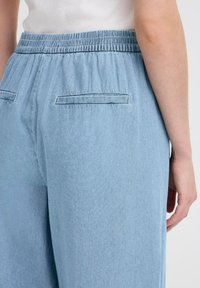 Svetlo modre hlače z elastičnim pasom in sproščenim fitom. Imajo dve zadnji žepu s horizontalnim šivanjem. Mehka, denim podobna tekstura.