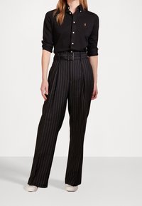 Black button-up shirt, paired with high-waisted black pinstripe trousers; includes a belt, and features a smooth, polished fabric.