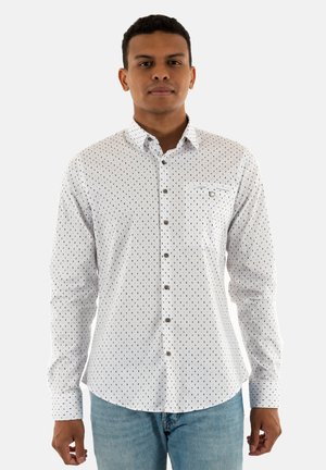 Chemise blanche à manches longues avec un col boutonné, dotée d'un motif à pois de couleurs sombres, d'une poche plaquée et de boutons marron.