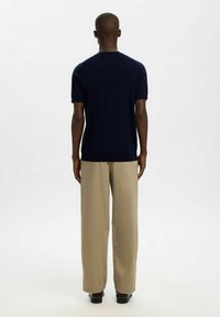 Pull en maille bleu marine à manches courtes avec un col rond, associé à un pantalon beige à jambes larges et à des chaussures noires, vu de dos.