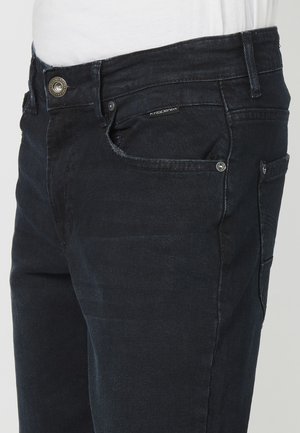 Jean en denim foncé avec une coupe droite, présentant une fermeture à bouton, des poches avant et arrière, et une étiquette de marque discrète.