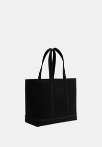 Sac cabas en toile noire avec deux longues poignées et couture renforcée au bas sur un fond clair uni.