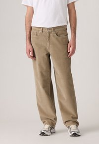 Beige corduroy trousers with a straight cut, featuring front pockets and a classic waistband, paired with gray sneakers and a white t-shirt.