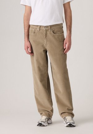 Beige corduroy trousers with a straight cut, featuring front pockets and a classic waistband, paired with gray sneakers and a white t-shirt.