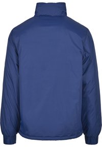 Tamsiai mėlyna pūkinė striukė su aukštu apykakle, elastingais rankogaliais ir lygiu, lengvu išoriniu paviršiumi. Paprastas, nepuoštas nugaros dizainas.