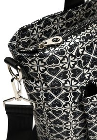 Černobílá taška s motivem srdce, vybavená zipovým uzávěrem, lesklými stříbrnými prvky a odnímatelným popruhem. Vyrobená z hladké látky.