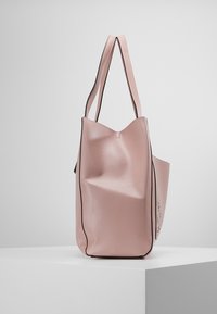 Skórzana torba typu tote w delikatnym różowym kolorze z fakturowaną powierzchnią, wydłużonymi rączkami oraz wysokim, usztywnionym kształtem z czarną lamówką wzdłuż krawędzi.