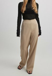 Pantalons taille haute beige avec une finition lisse et des jambes larges, associés à un haut noir à manches longues. Présente des lignes épurées et des accents minimalistes.