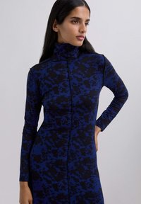 Abito a maniche lunghe con colletto alto, di colore blu scuro con motivi a macchie nere, realizzato in un tessuto morbido e elastico.
