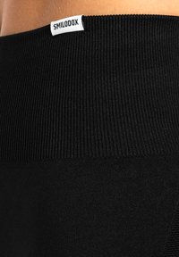 Leggings neri con una vita a coste e un'etichetta bianca. Tessuto liscio senza pattern o dettagli aggiuntivi.