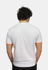 T-shirt bianco a maniche corte con accenti a costine arancioni sui polsini e sul colletto. Il tessuto sembra liscio e aderente.