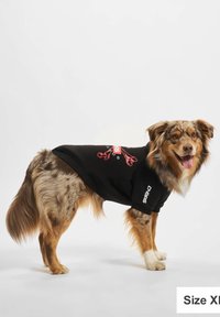 Svart hundegenser med korte ermer, med et rødt grafisk design. Hunden har en flekket pels med lysebrune og kremfargede nyanser. Størrelse XL.
